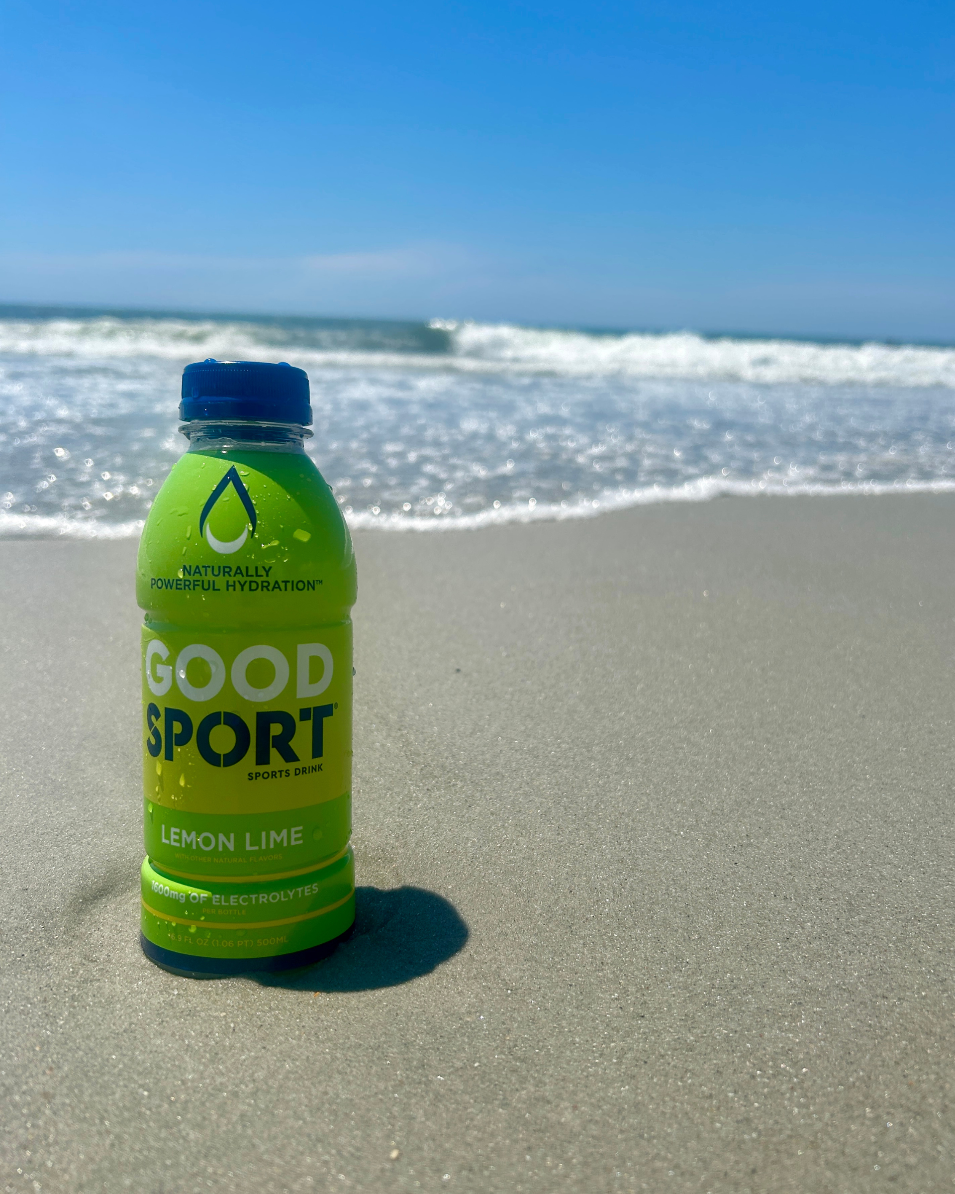GoodSport lemon lime sports drink bottle on a sandy beach with ocean waves in the background