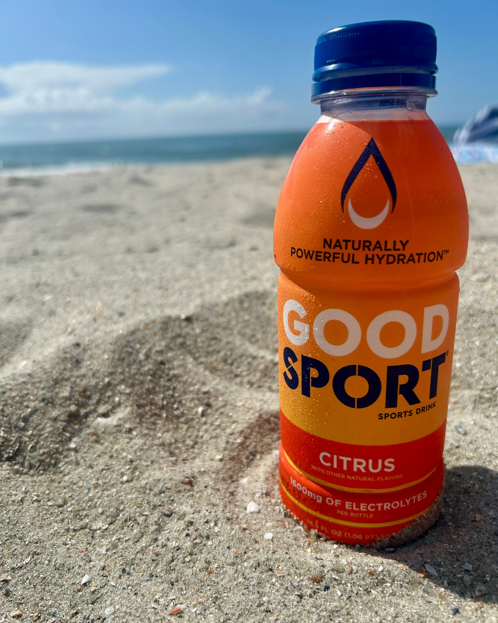 GoodSport citrus sports drink bottle on a sandy beach with ocean view