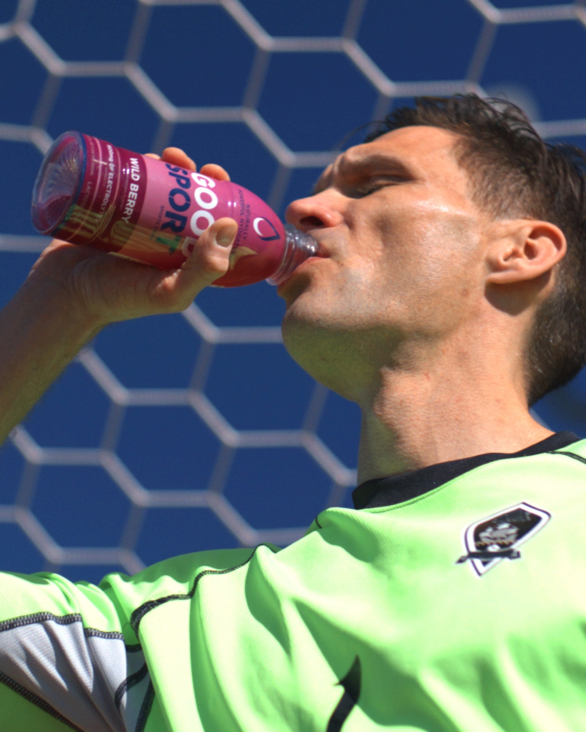 Soccer player drinking Wild Berry GoodSport on a soccer field.