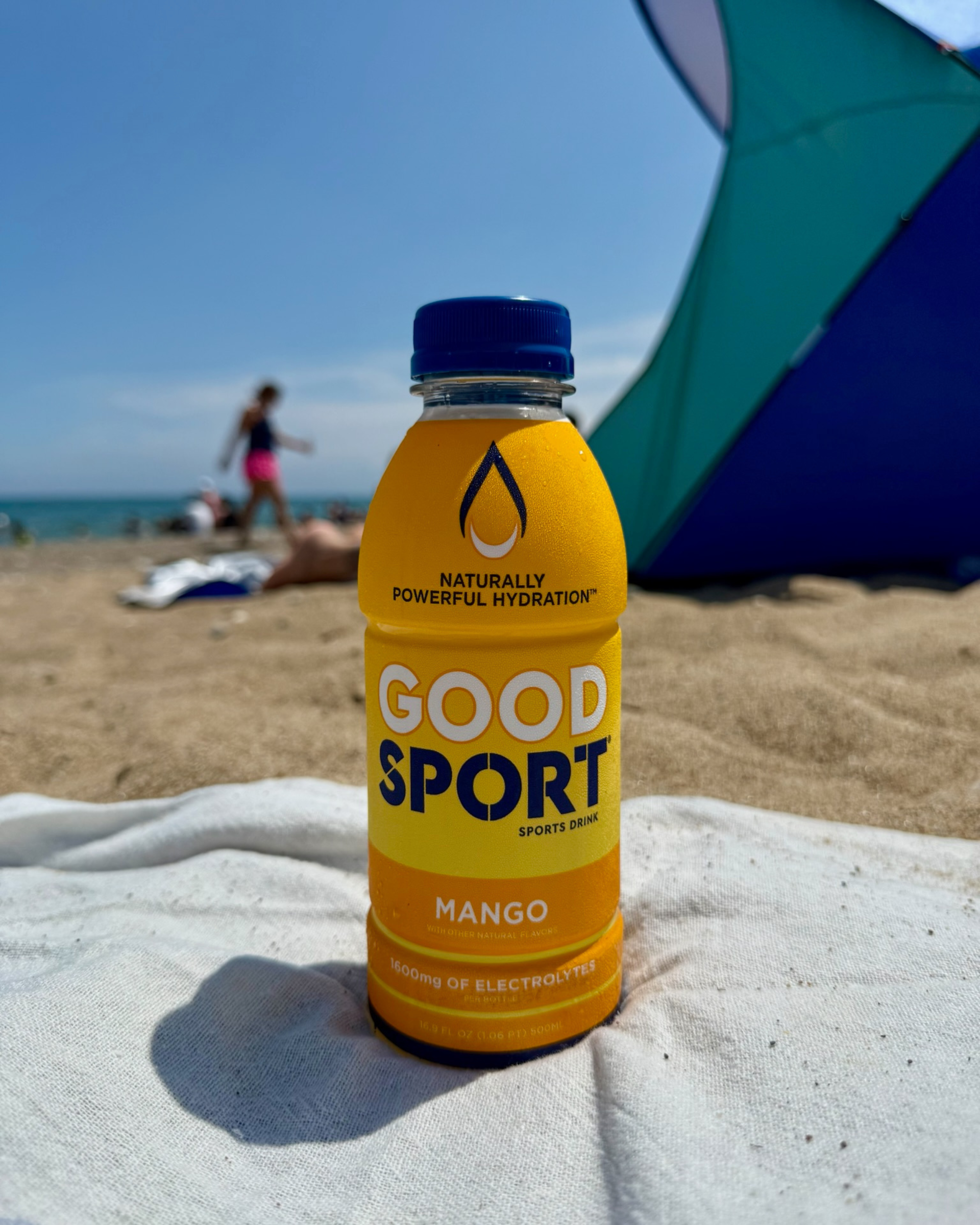 Mango GoodSport sports drink bottle on a beach with people and an umbrella in the background