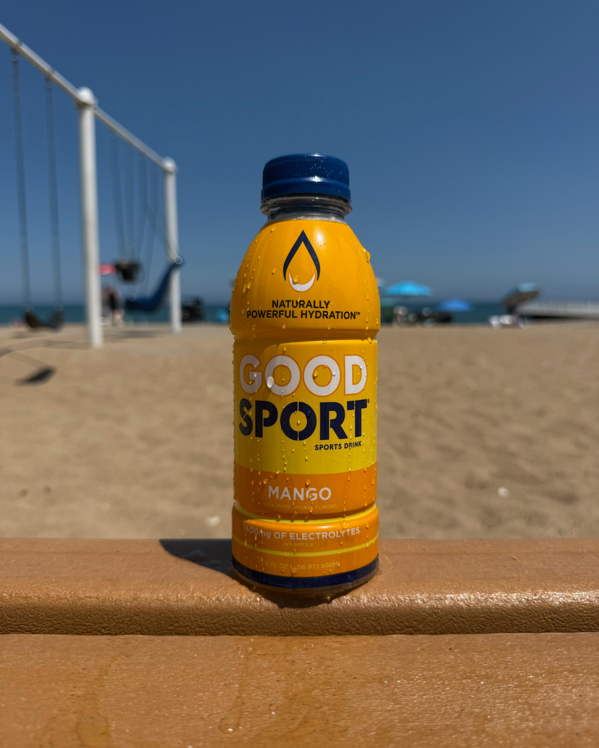 A bottle of Mango GoodSport sports drink bottle on a beach.