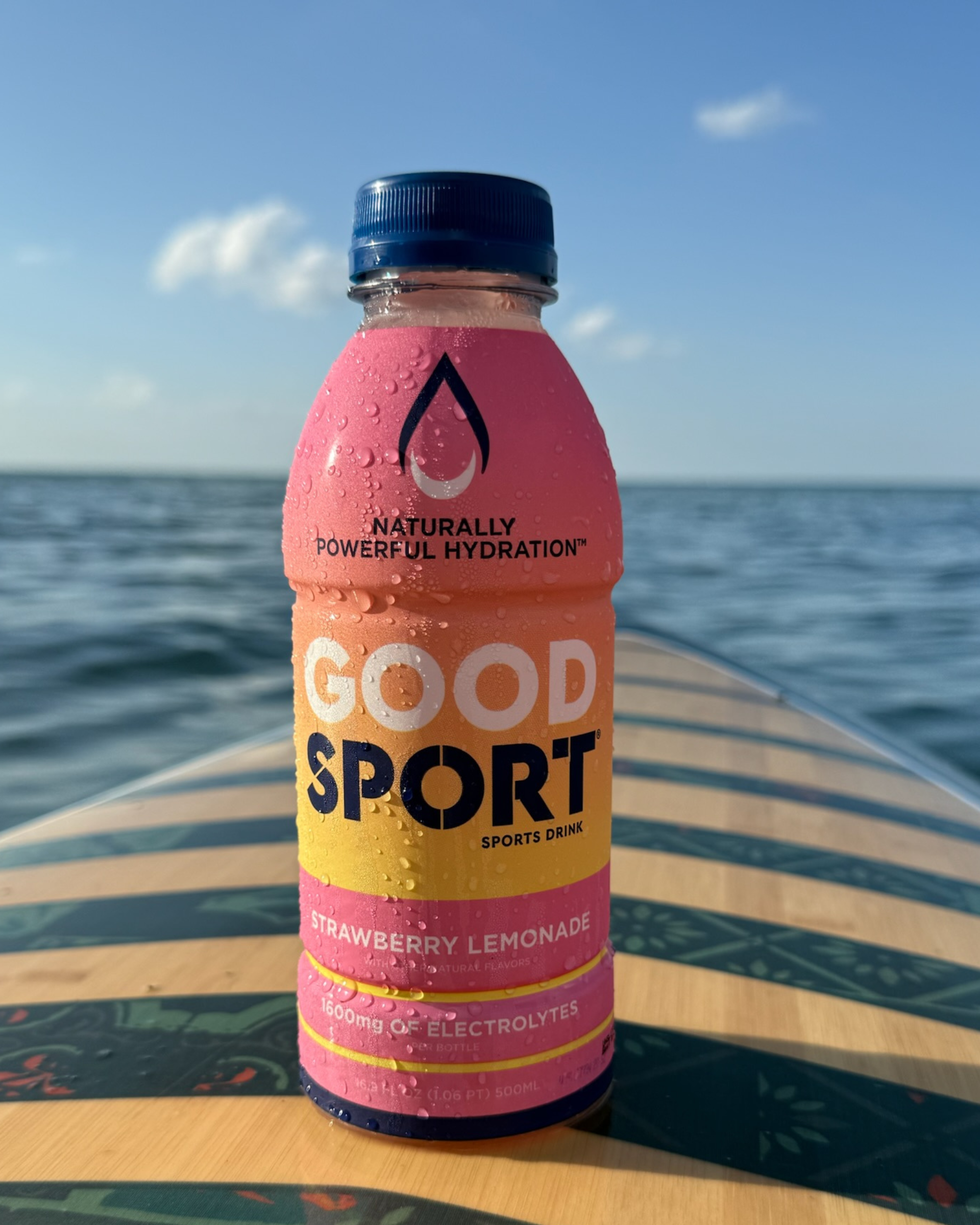 Strawberry Lemonade GoodSport sports drink bottle on a surfboard with ocean background
