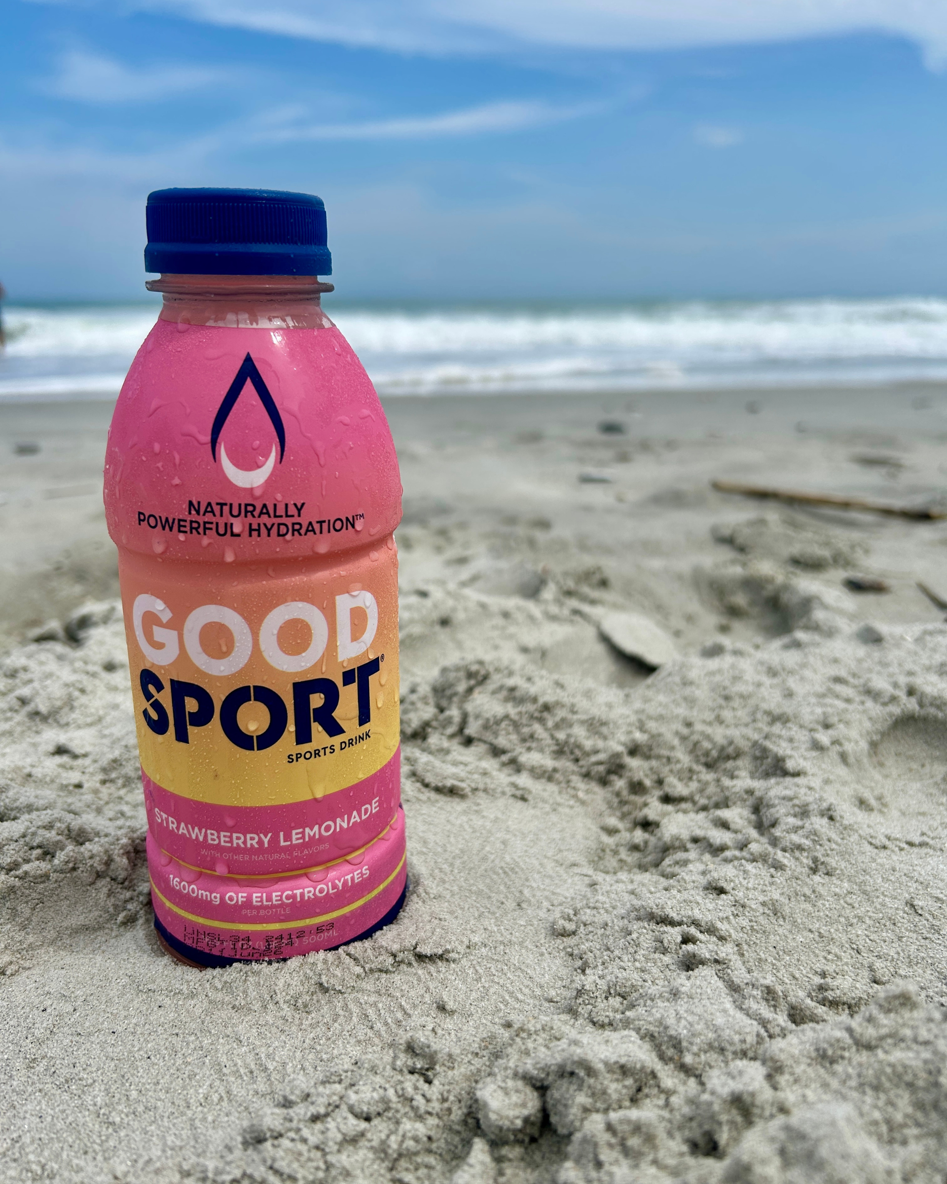 Strawberry Lemonade GoodSport sports drink bottle on a sandy beach with ocean in the background