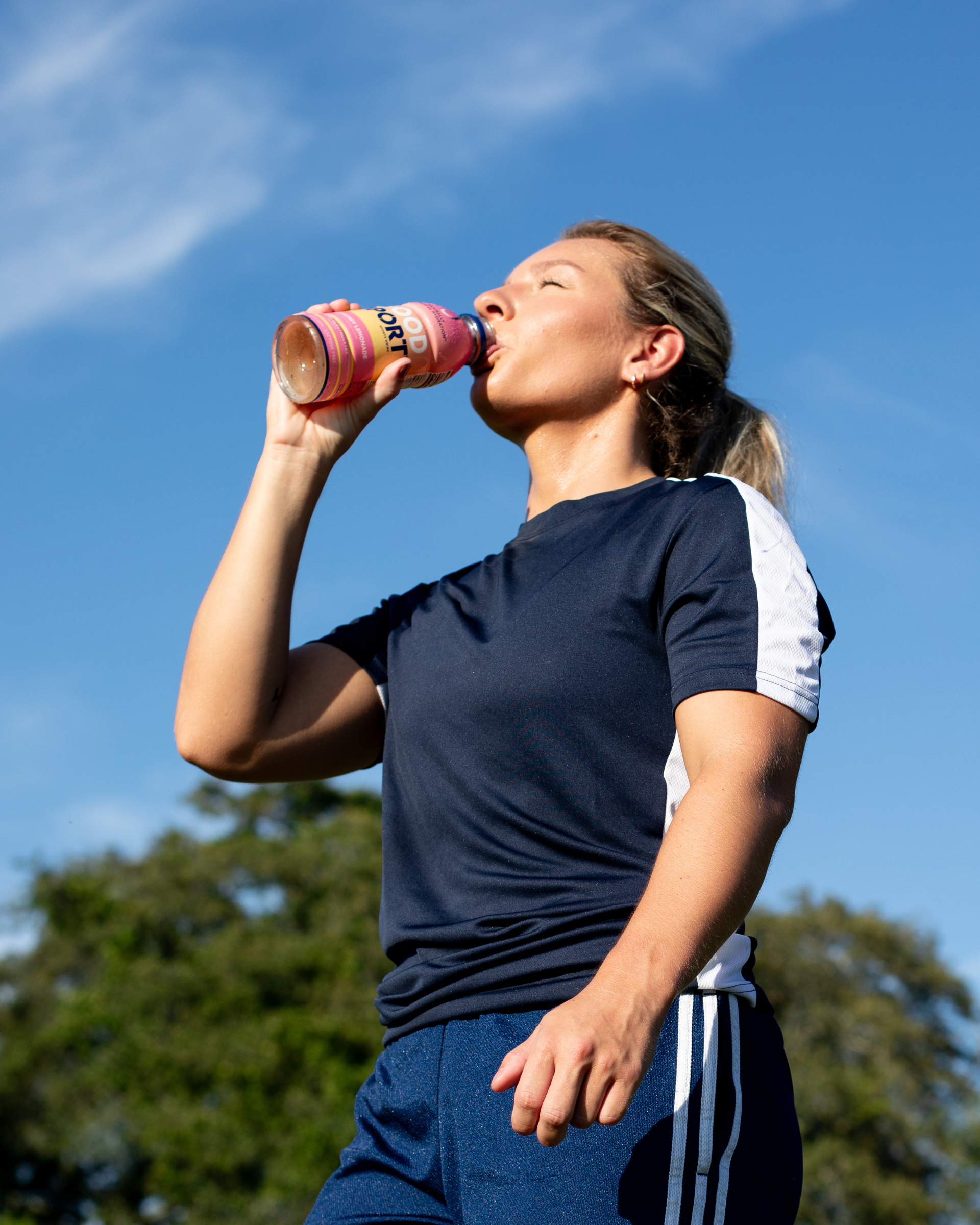 Soccer Player drinking Strawberry Lemonade in front of blue sky and trees