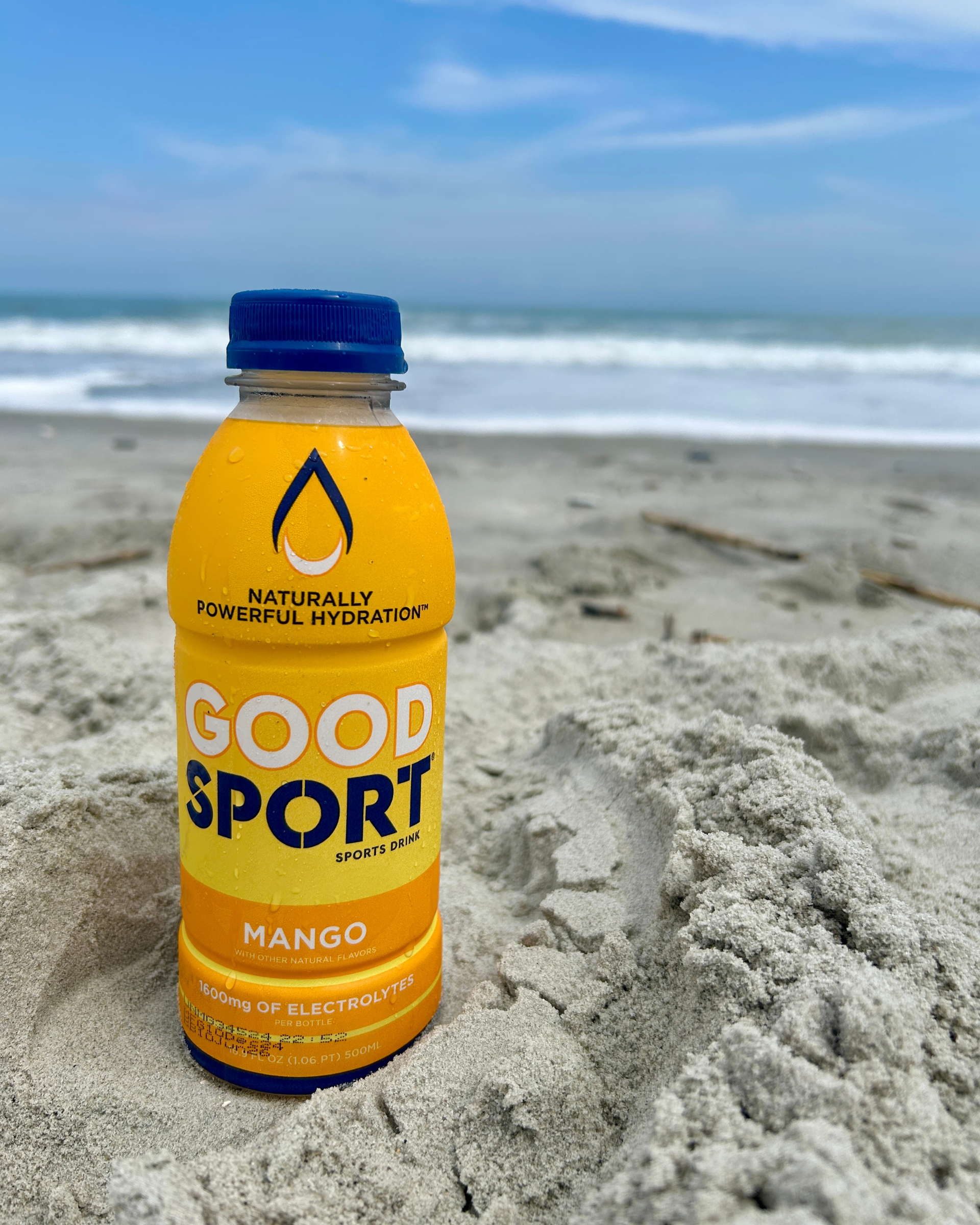 Mango GoodSport sports drink bottle on a sandy beach with ocean in the background