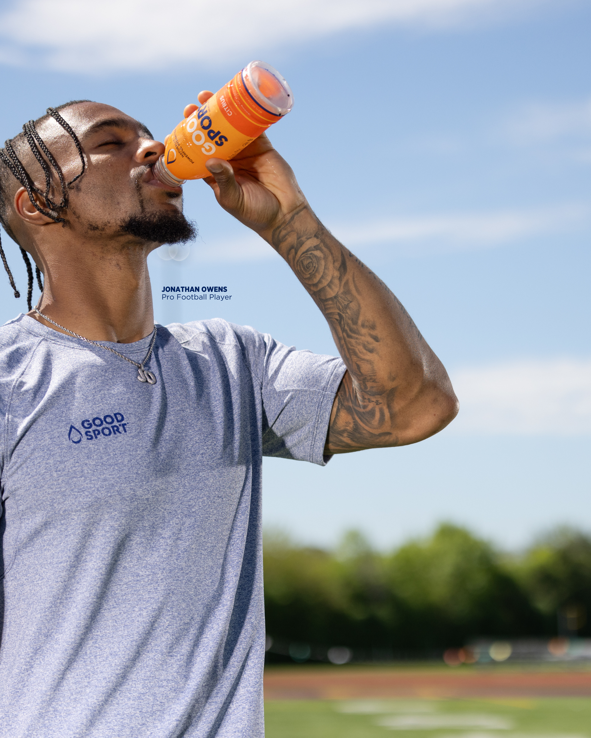 Pro football player Jonathan Owens standing on the football field drinking a bottle of citrus GoodSport sports drink.