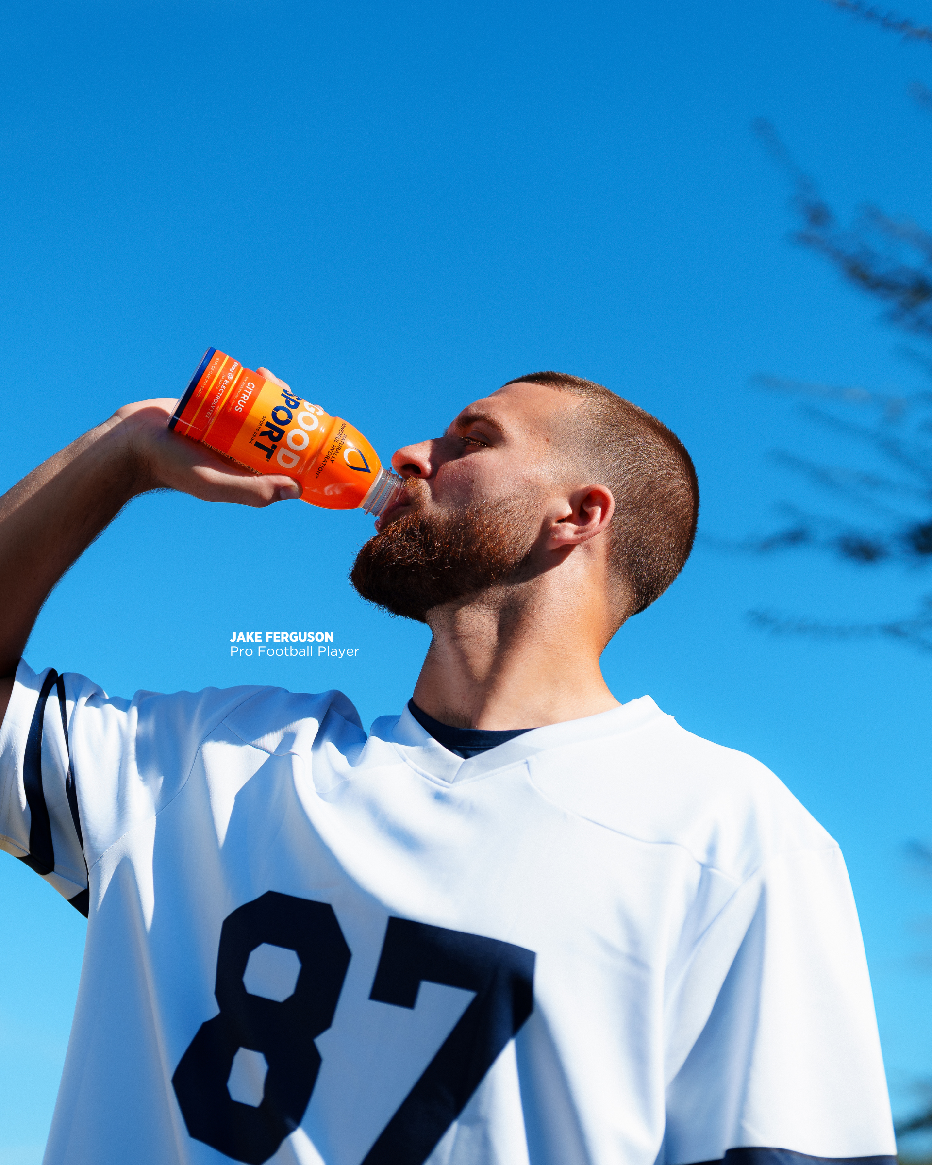 Pro football player Jake Ferguson on field drinking bottle of Citrus GoodSport sports drink.
